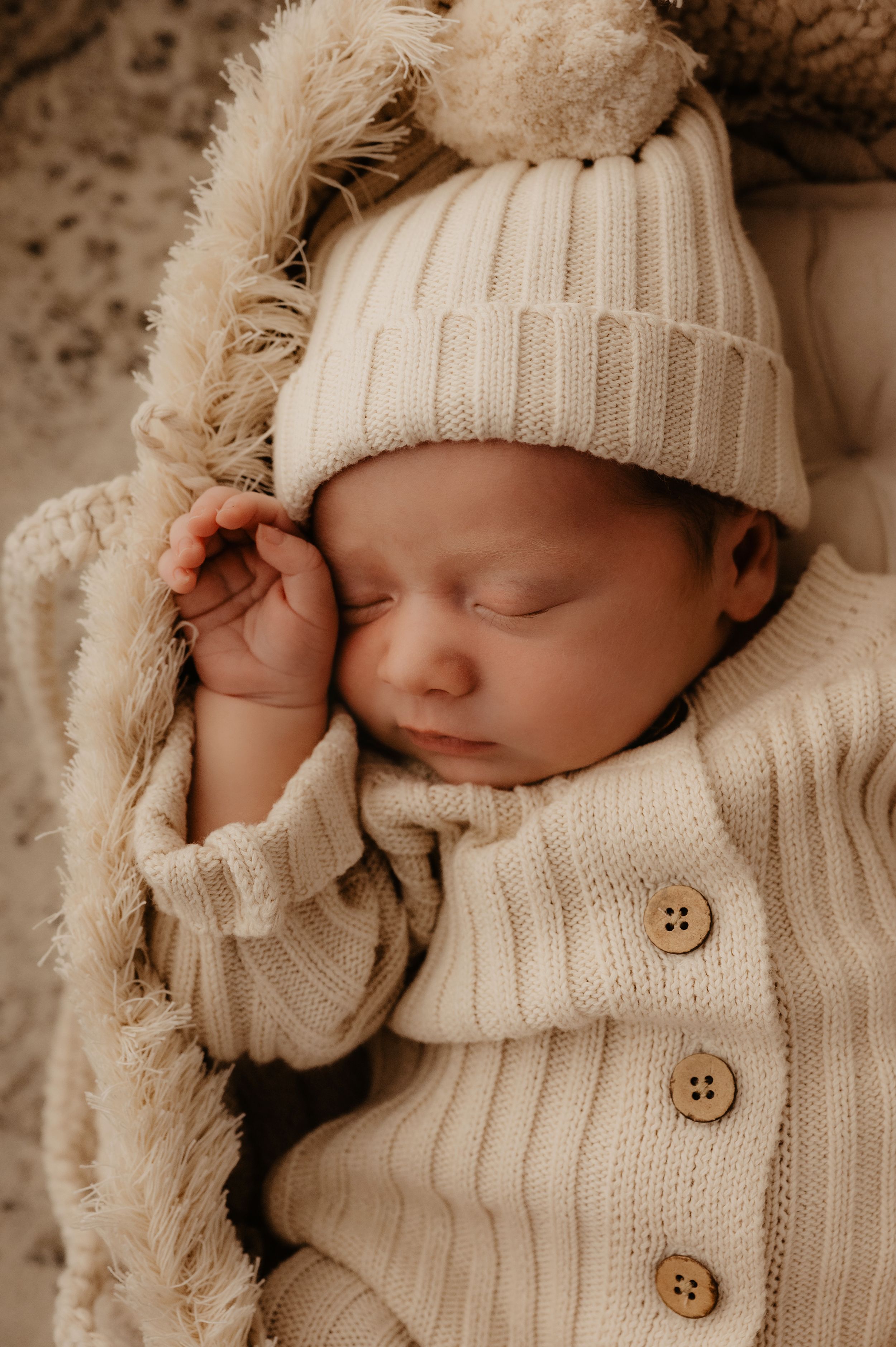 Sleeping newborn wearing knit sweater and beanie in cream colors.