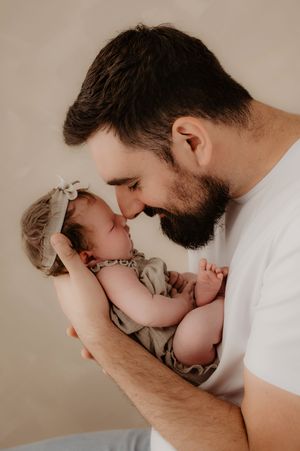 Tender moment between father and newborn baby against neutral background.