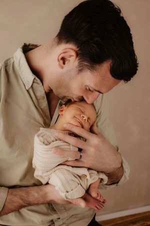 Tender moment between parent and infant in soft beige tones.