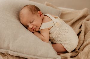 Peaceful sleeping baby wrapped in knit blanket on neutral bedding.