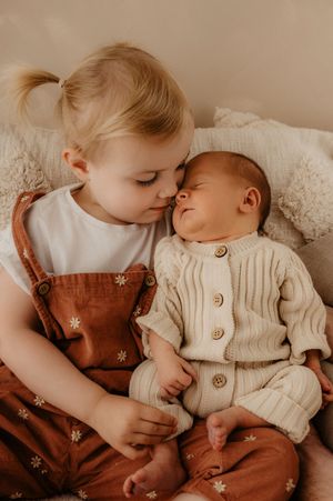 Two children in vintage-style clothing sharing tender moment on beige background.