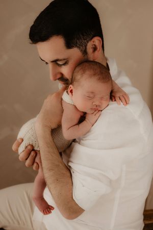 A tender moment captured of a parent in a white shirt cradling a sleeping newborn against their chest.