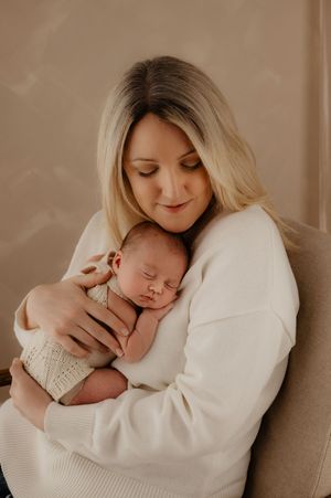 Intimate newborn portrait with parent in white sweater holding sleeping baby in soft natural light.