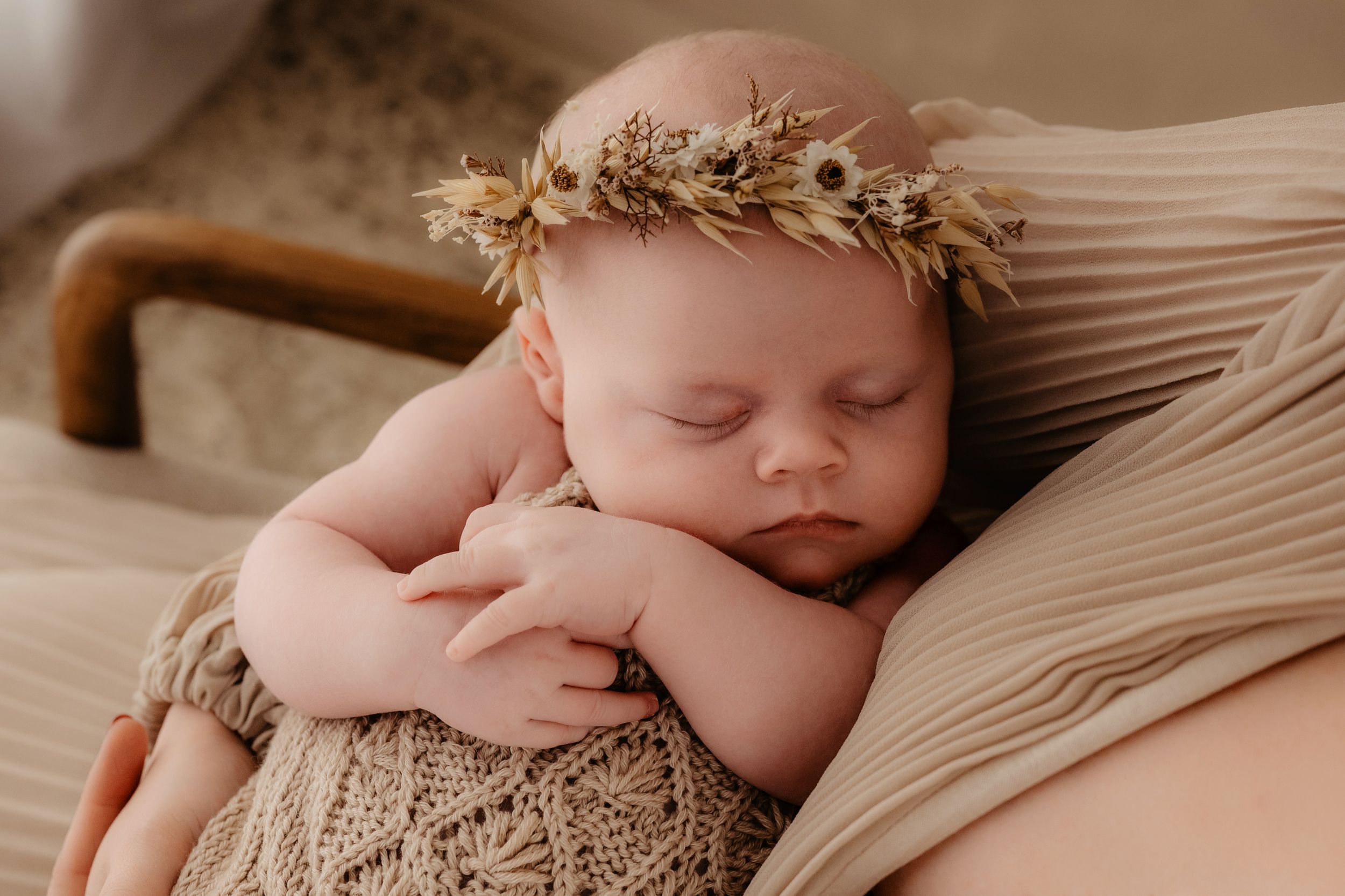 A sleeping newborn baby lies peacefully on beige fabric in a warm-toned photography series.