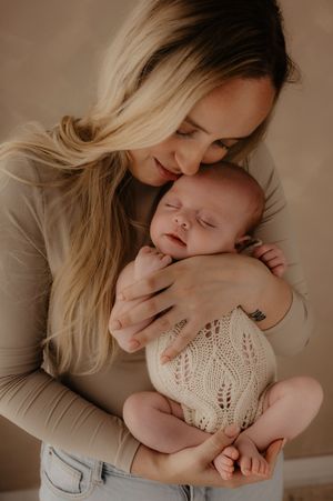 A tender moment captured in warm tones as a mother snuggles with her sleeping baby wearing delicate lace clothing.