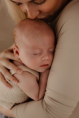 A peaceful sleeping newborn baby nestles close in a warm embrace wearing a soft knit outfit.