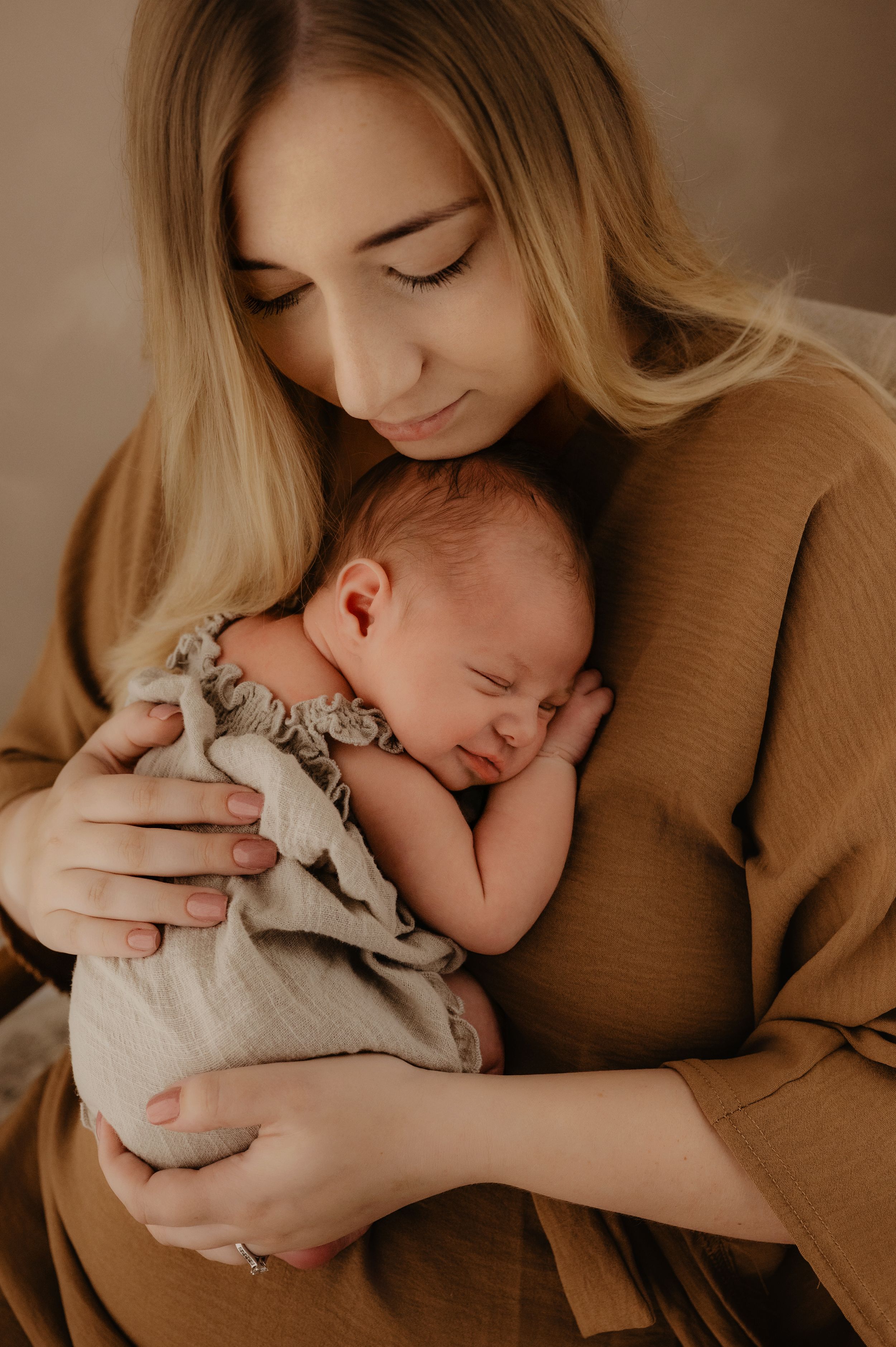 Sweet newborn photography series in warm brown tones shows tender moments between parent and sleeping baby.