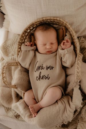 Newborn baby wearing cream colored outfit laying on textured fabric.