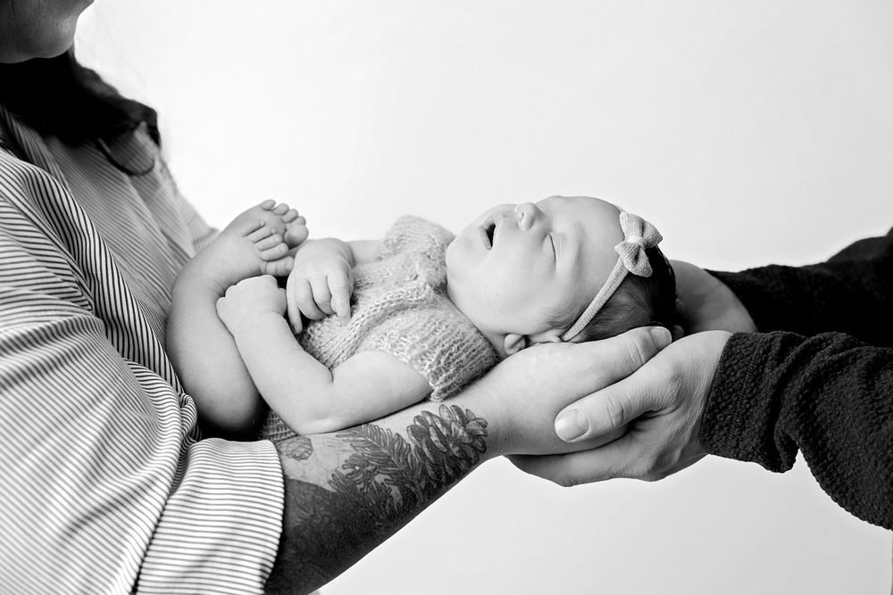 Black and white photo of newborn baby being cradled in parents hands.