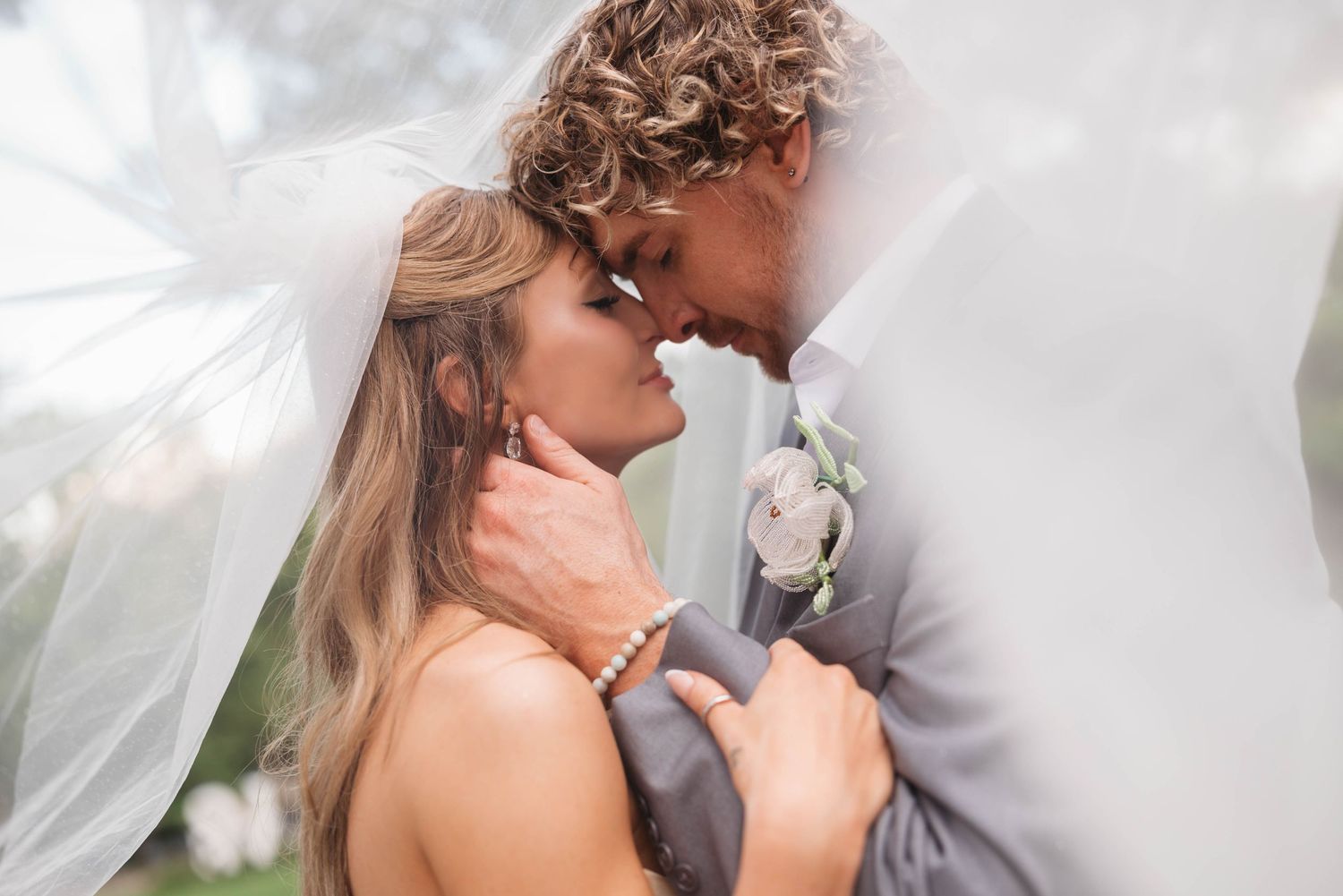 Elegant wedding couple shares an intimate moment under a flowing white veil.