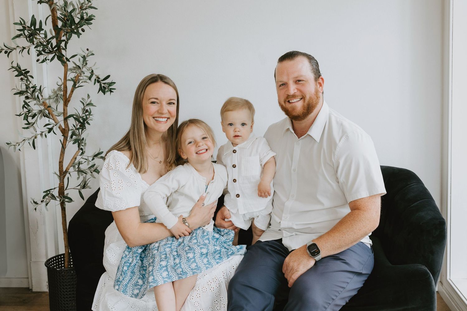 Modern family portrait in white room with black accent furniture.