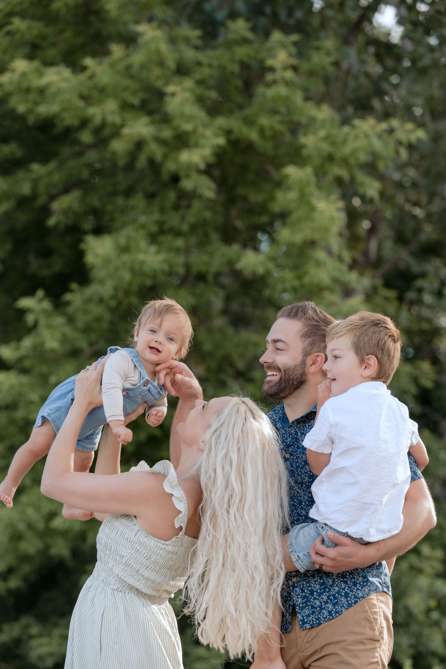 family holds their baby lovingly in the air to celebrate his first birthday during a beachy outdoor lifestyle session in hudson wi