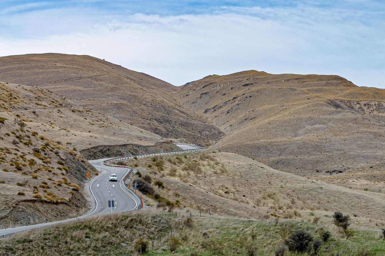 A lone white house sits along a winding road through barren brown hills.