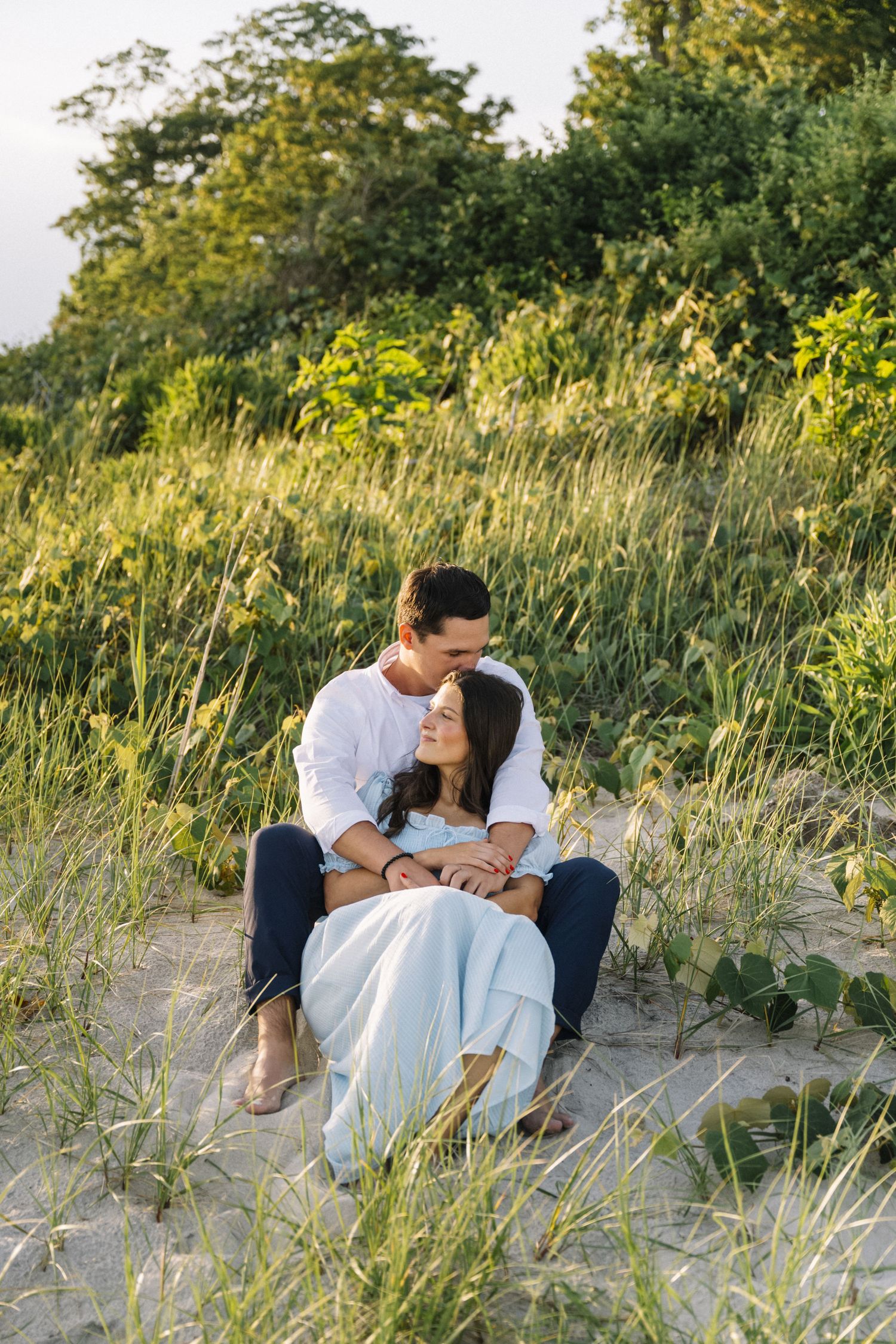 A romantic couple embraces and laughs together during a sunset engagement by the water in New York City