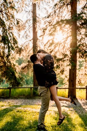 Playful couple embracing in golden sunset light among tall pine trees.