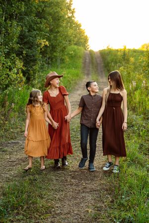 A family walks together on a sunlit nature path wearing coordinated burgundy and brown autumn outfits in golden light.