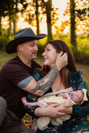 Family shares intimate moments with newborn baby outdoors during golden hour sunset.
