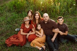 People posing in coordinated rust and mustard colored outfits for outdoor family portraits amidst greenery.