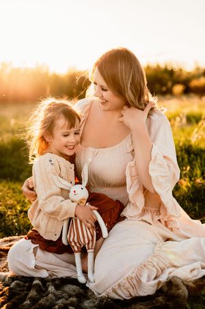 A tender moment captured at golden hour as parent and child share laughter while sitting in a sunlit meadow.