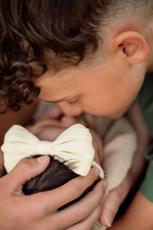 Close-up of baby with white bow being gently cradled during outdoor photo session.
