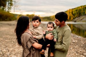 A family enjoying a peaceful moment together along a rocky lakeshore at sunset with autumn trees in the background.