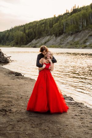 A flowing red ball gown creates a stunning contrast against the sandy beach at sunset with forest in the background.