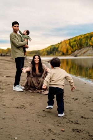 Family spending time together on a sandy beach by a lake surrounded by fall foliage on an autumn day.
