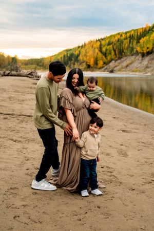 A family enjoys an autumn day together on a beach beside a scenic lake with golden-leaved hills in the background.
