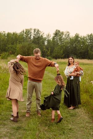 Family enjoying playful moment together in grassy field on autumn day wearing earth-toned clothing.