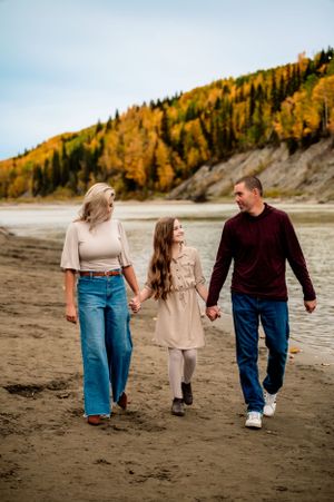Family walking on a beach trail together during autumn with golden trees on hillside in background.