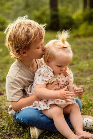 Two young children share a sweet moment together while sitting outdoors in a natural setting.