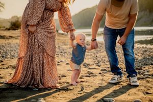 People walking along a sandy beach at sunset holding hands with their small toddler.