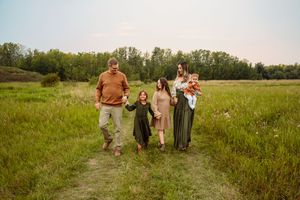 Family group walks together on a dirt path through a green meadow during a sunny summer day.