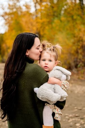 A tender autumn moment between parent and child outdoors with golden foliage in the background.