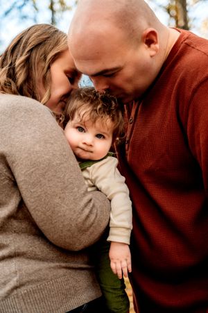A tender family moment captured outdoors as parents share an intimate embrace with their young child.