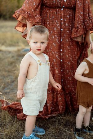 Small toddler wearing white top and blue shorts exploring outdoors in golden sunlight.