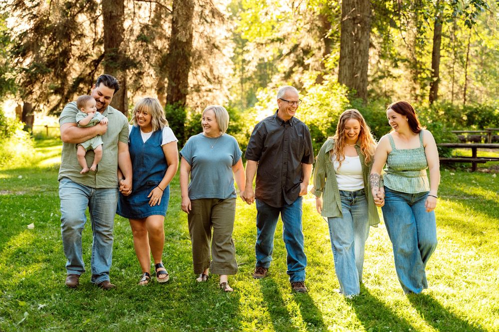 Multi-generational family walking together in a sunny green park, smiling and holding hands on a warm day.