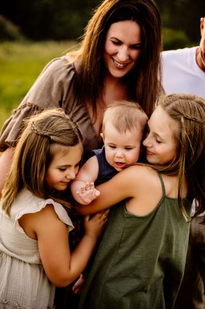 A happy family moment captured outdoors as they share affectionate hugs and smiles in natural lighting.