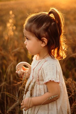 A child in a white dress backlit by golden sunset light while playing in a field of tall grass during golden hour.