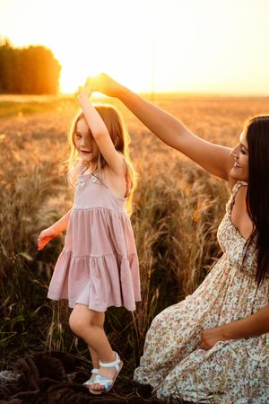 A mother and child share tender moments in a golden wheat field at sunset wearing flowy dresses.