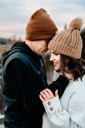 Couple in winter beanies sharing an intimate moment outdoors during sunset.