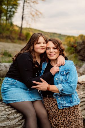 Two friends embrace while sitting on rocks during an autumn photoshoot, wearing denim and animal print.