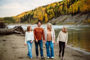 Group walking along a scenic autumn riverbank with golden trees reflecting in the calm water.
