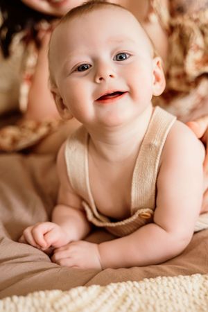 Happy smiling baby in beige romper lies on stomach looking up with bright blue eyes.