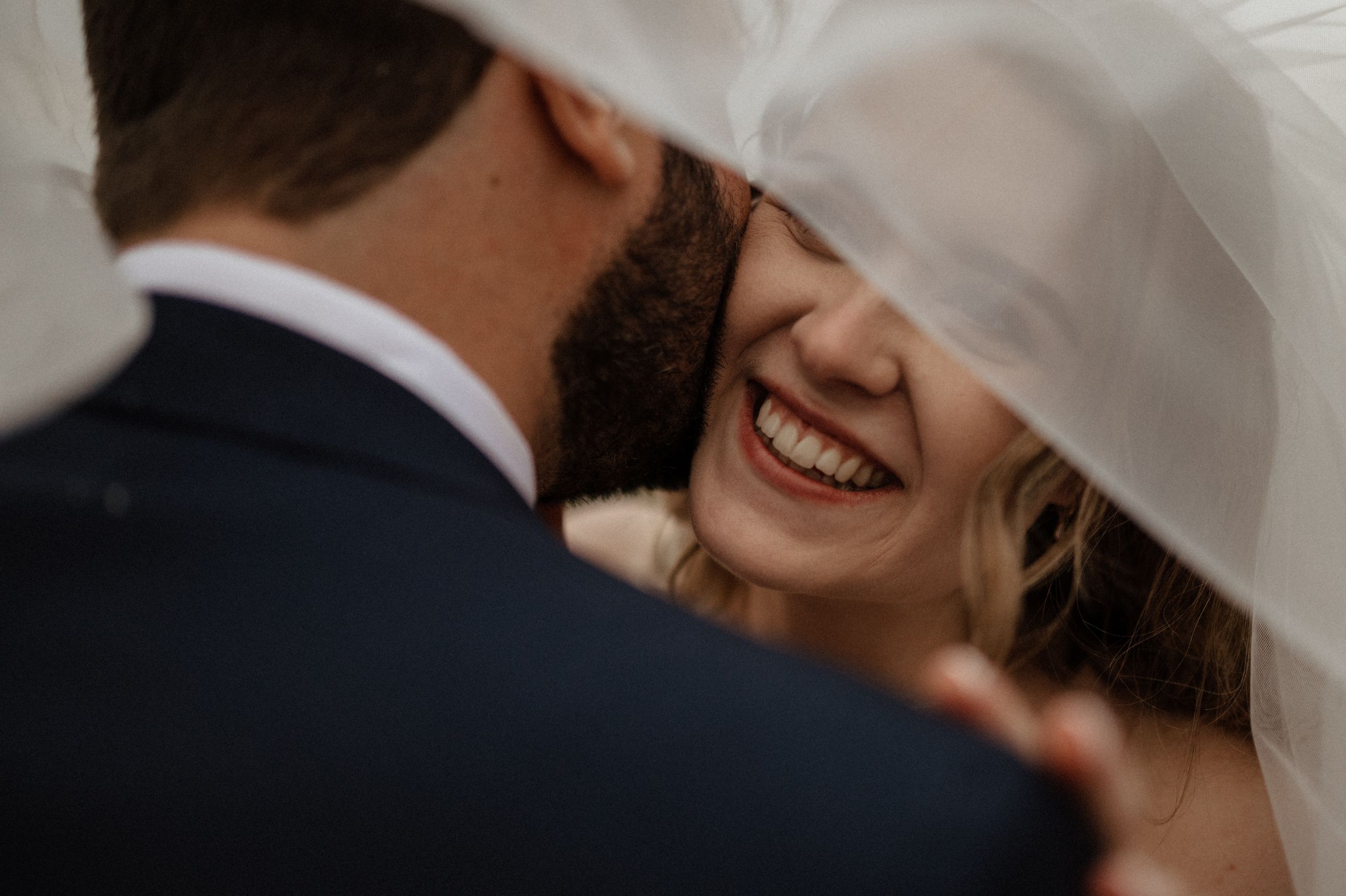 Close-up of joyful intimate moment under white bridal veil.