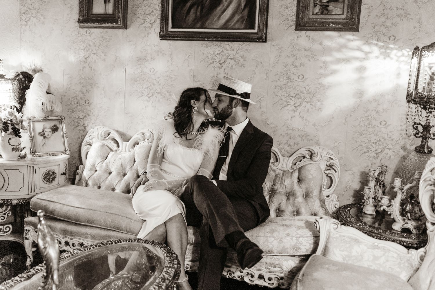 Couple in elegant attire sharing a kiss on an ornate vintage sofa in a romantic room with damask wallpaper and antique decor.