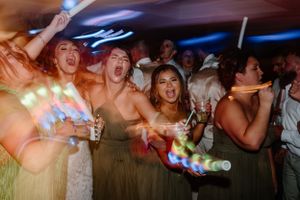 Wedding guests dancing enthusiastically at a reception with colorful party lights.