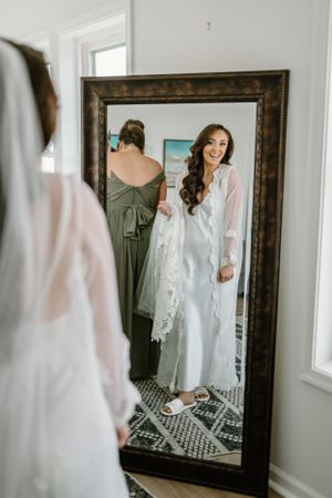 A reflection in a full-length mirror shows a white satin robe and lace wrap with patterned tile flooring beneath.