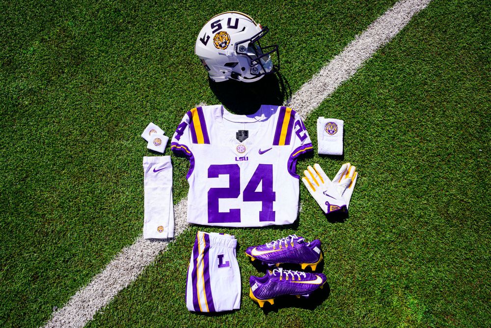 LSU football uniform and equipment layout including purple cleats and white jersey on grass field.
