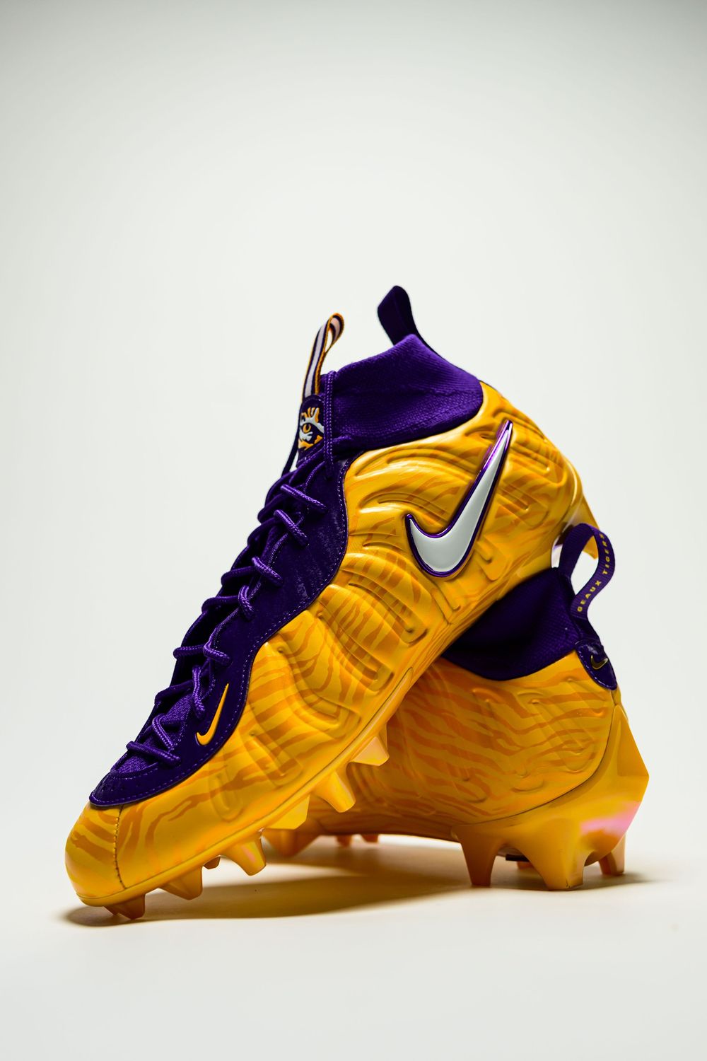 Pair of gold and purple Nike football cleats with a white swoosh, purple laces and molded studs, stacked against a plain white background.